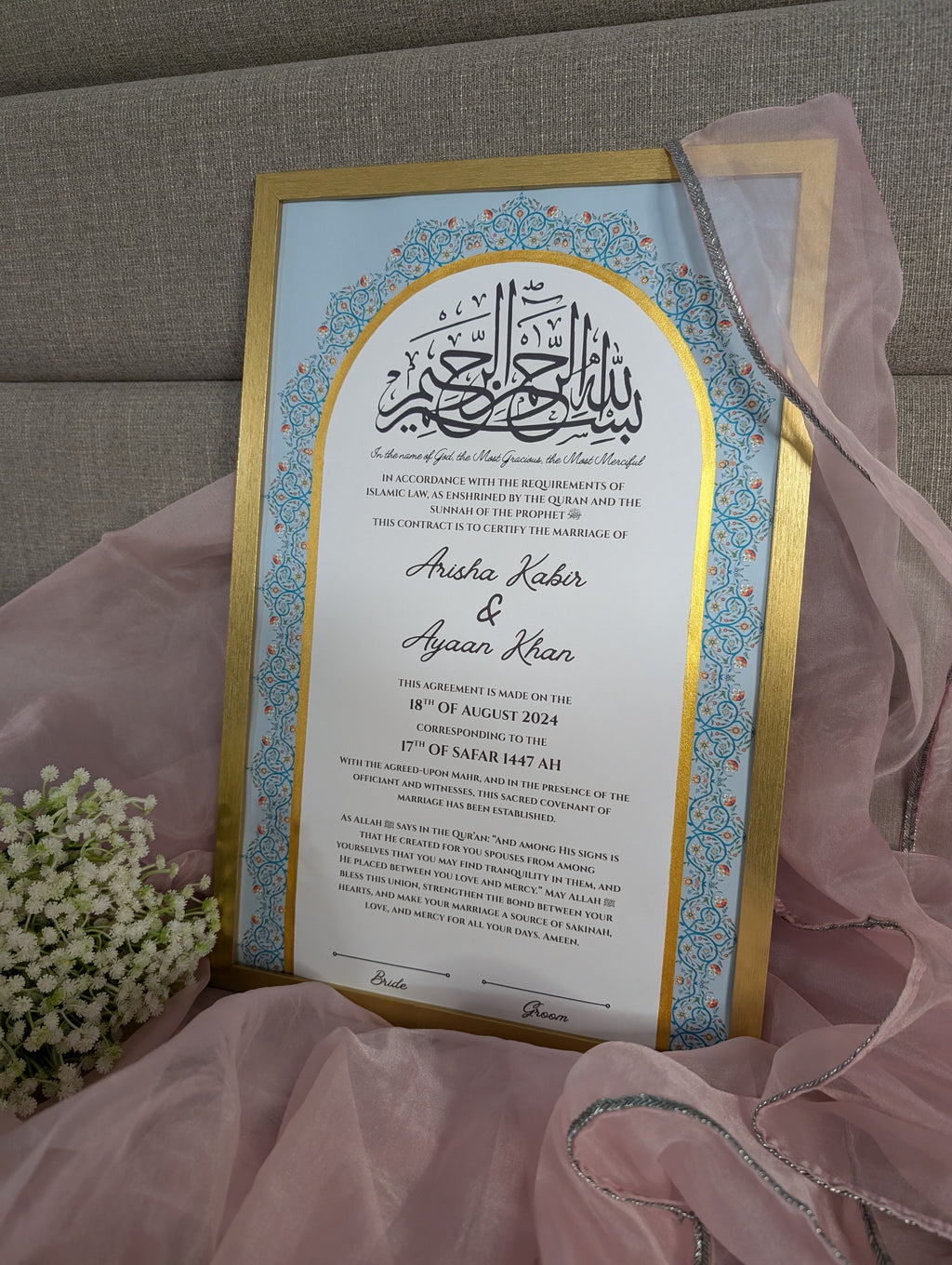 Decorative wedding invitation card with gold and blue border on a pink fabric background